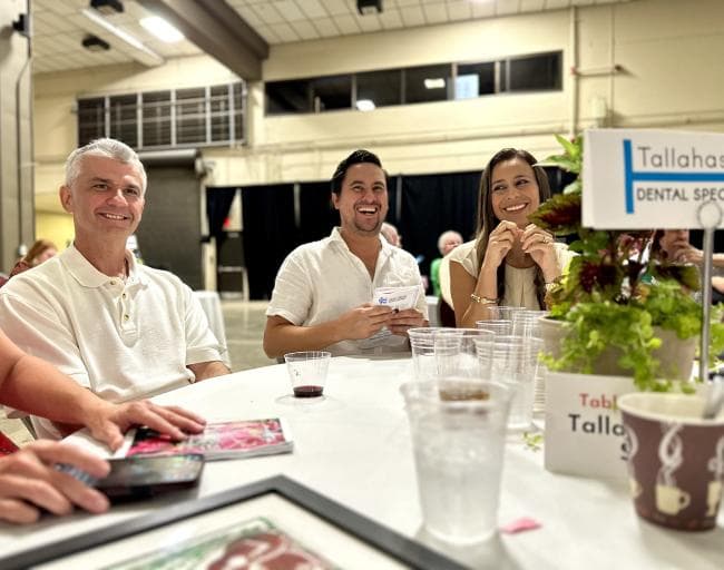 Three individuals laughing while sitting at a round table at an event. 
