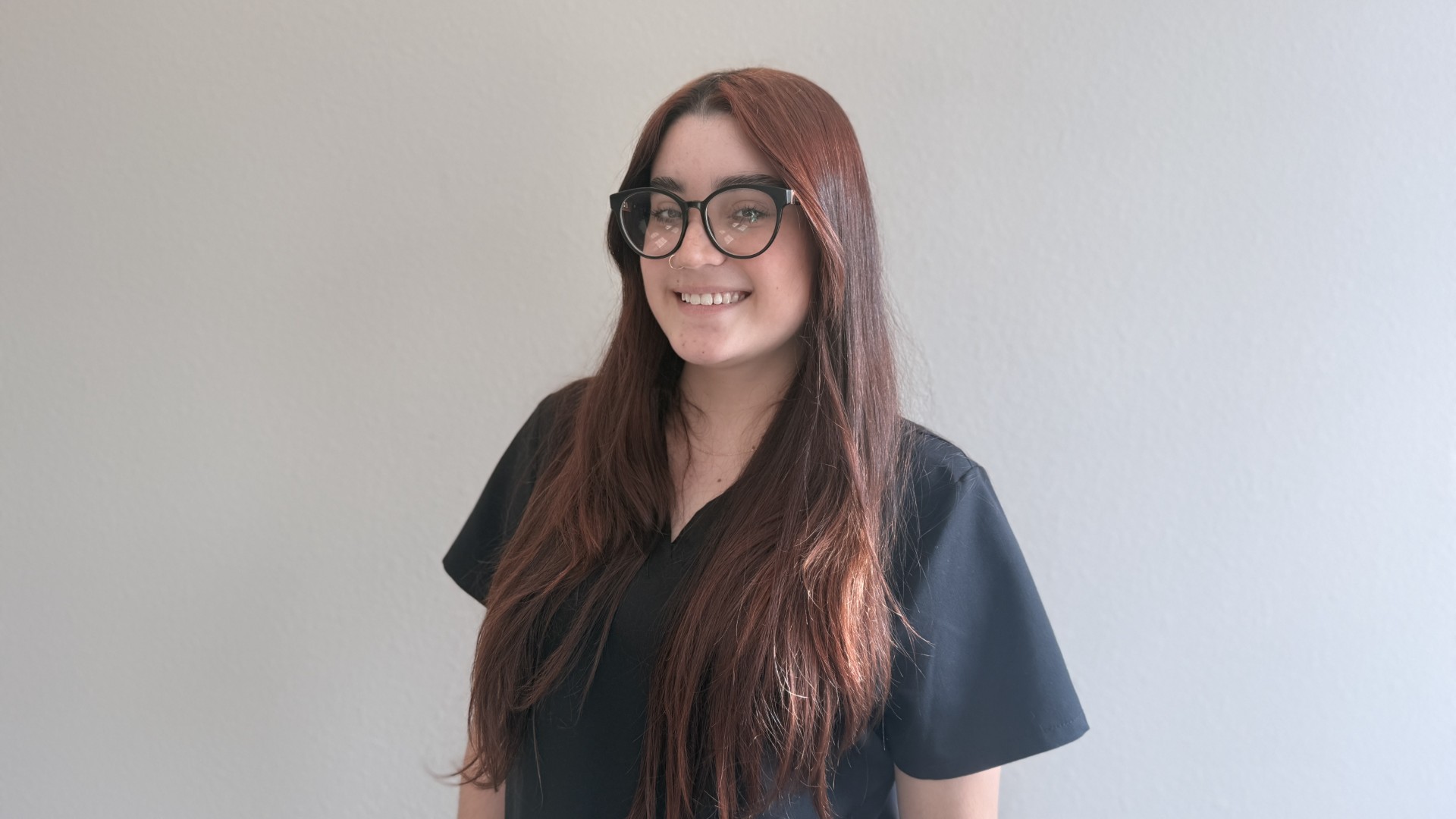 A person smiling while standing up against a blank wall