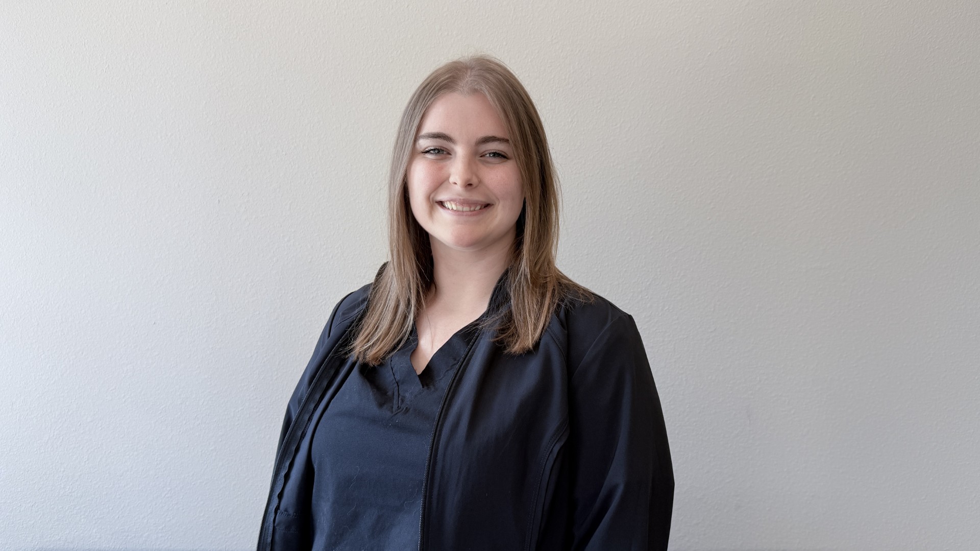 A person smiling while standing up against a blank wall