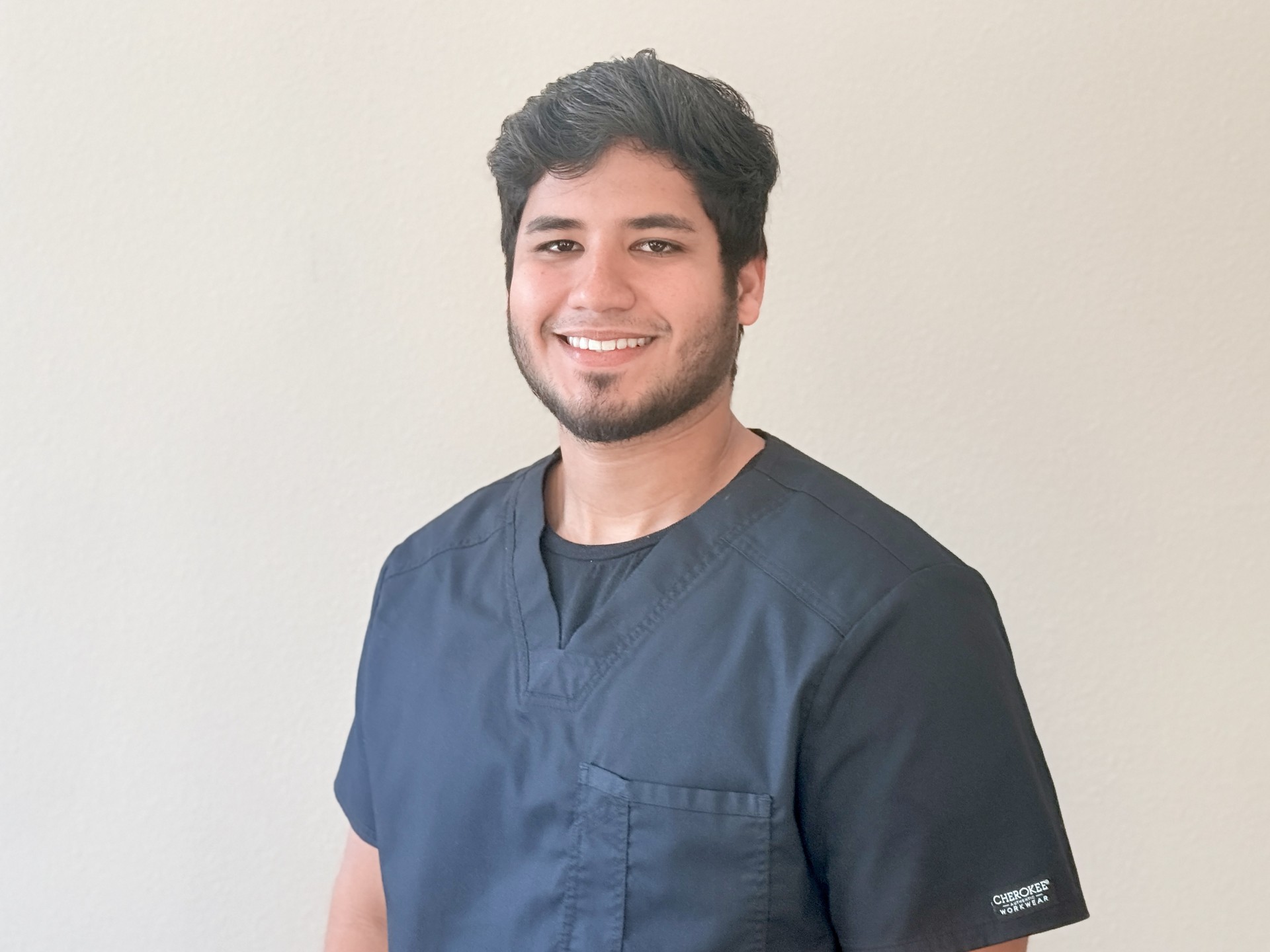 A person smiling while standing up against a blank wall