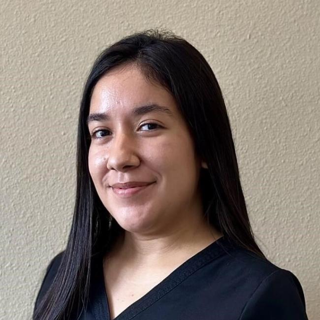 Dental team member smiling while standing up against a blank wall