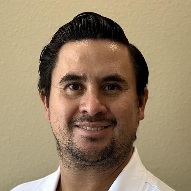 Prosthodontist Dr. Galindo smiling, standing against a blank wall.