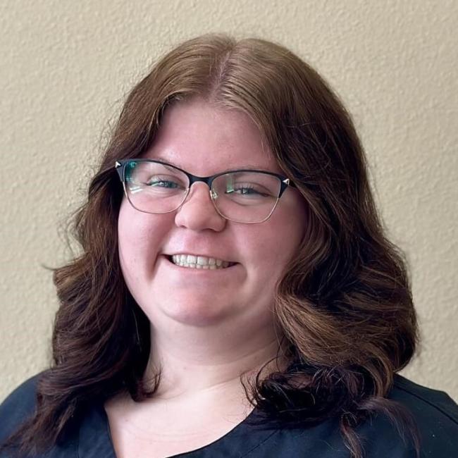 A dental team member smiling while standing against a blank wall.