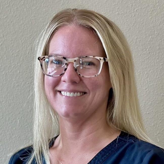 A dental team member smiling while standing against a blank wall.