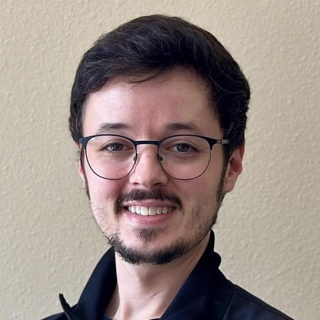 A dental team member smiling while standing against a blank wall.