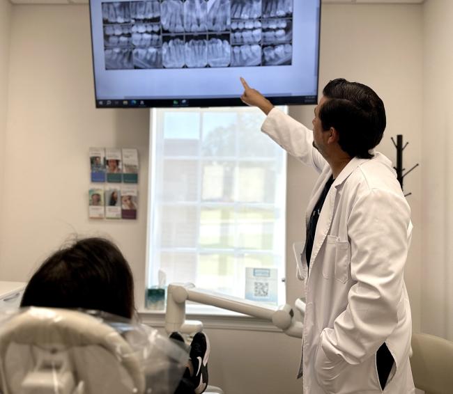 Dr. Galindo pointing to a screen with dental x-rays displayed. 