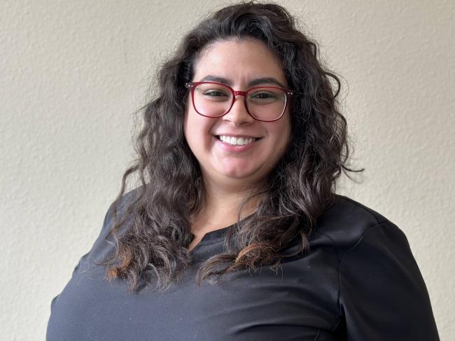 A person smiling while standing up against a blank wall