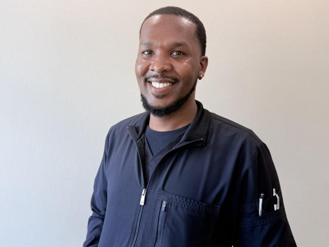 A person smiling while standing up against a blank wall