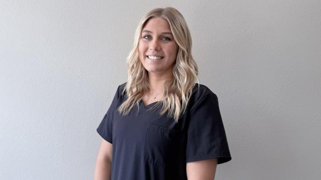 A person smiling while standing up against a blank wall