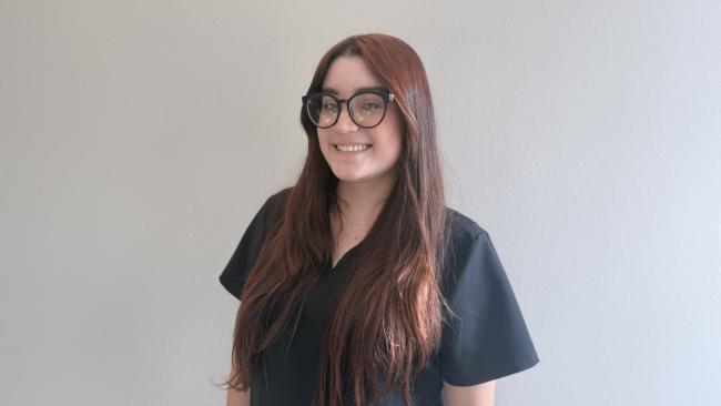 A person smiling while standing up against a blank wall