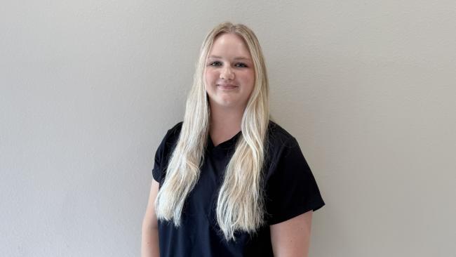 A person smiling while standing up against a blank wall