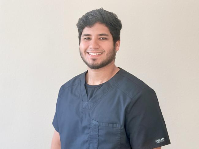 A person smiling while standing up against a blank wall